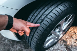 man inspecting the tread on his tire before determining if he needs to replace it