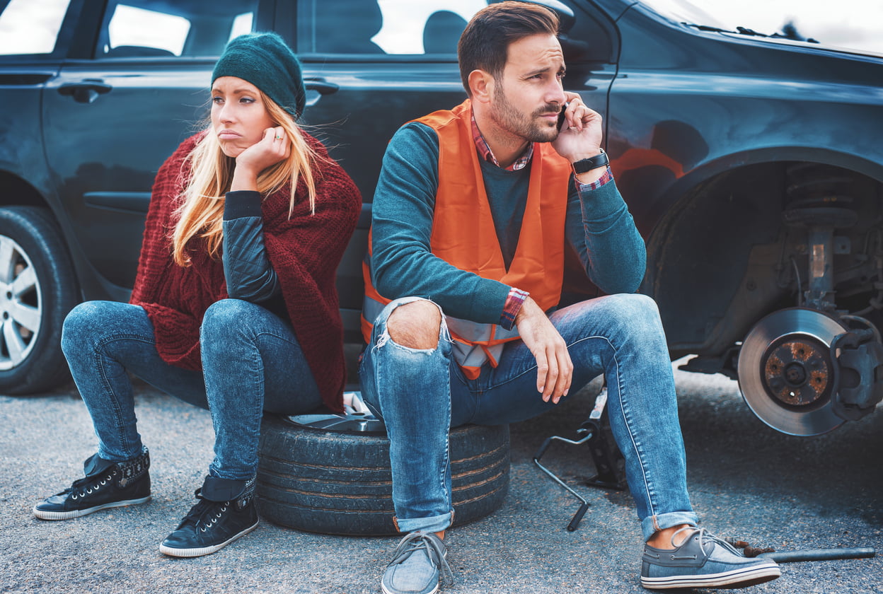 A couple on the side of the road dealing with a flat tire, one of the most common car issues you could experience.