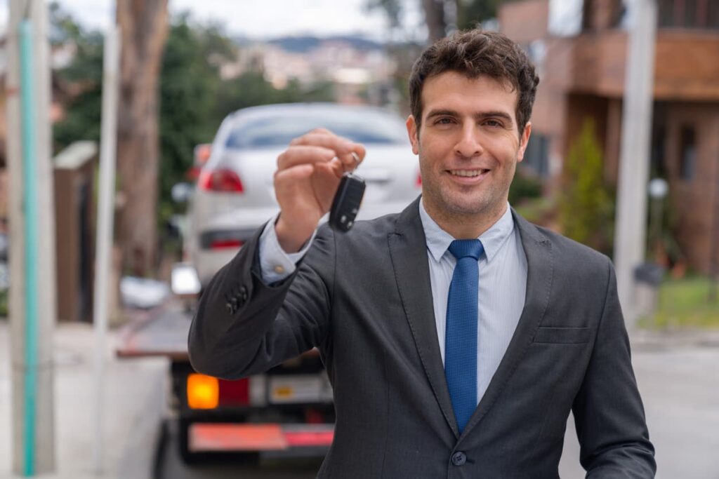 Man holding vehicle keys with car in background after the completion of a door-to-door car shipping transaction.
