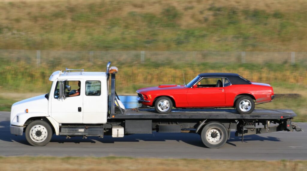 A flatbed tow truck with a classic car during the ship a non-running car process.
