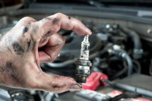 A mechanic holding up a dirty spark plug while completing a car tune-up.