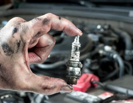 A mechanic holding up a dirty spark plug while completing a car tune-up.