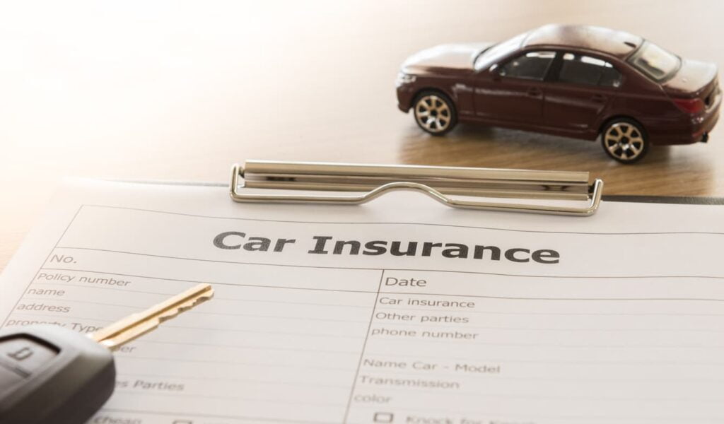 a vehicle, keys, and a car shipping insurance policy sitting on a desk.