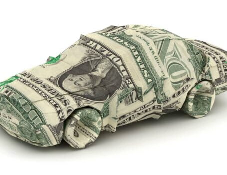 An origami car composed of one-dollar bills against a white background.