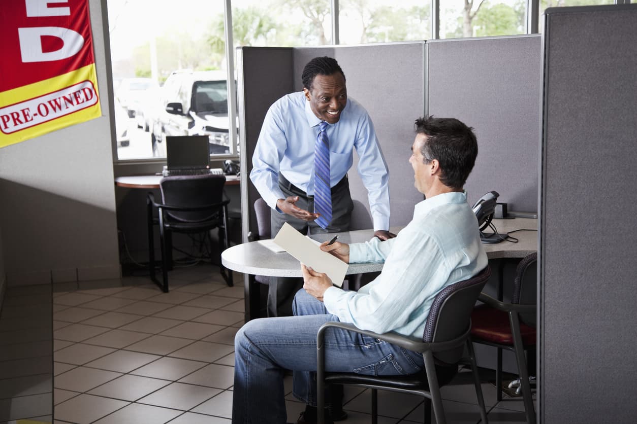 a customer going over some paperwork with a salesperson when buying a used car.