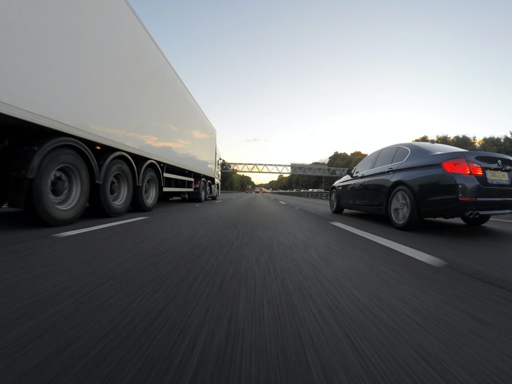Blue Infiniti Sedan Running on Road Together With White Freight Truck