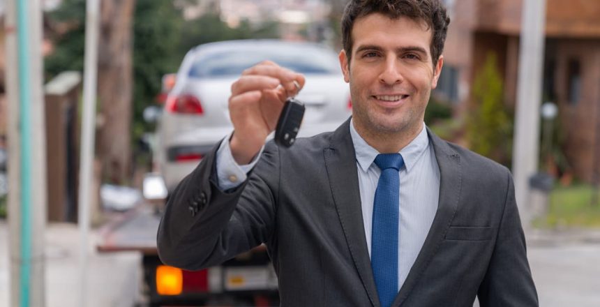 Man holding vehicle keys with car in background after the completion of a door-to-door car shipping transaction.