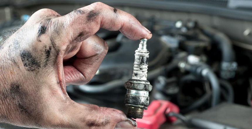 A mechanic holding up a dirty spark plug while completing a car tune-up.