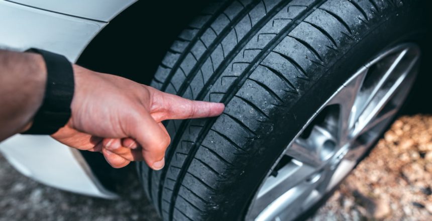 man inspecting the tread on his tire before determining if he needs to replace it