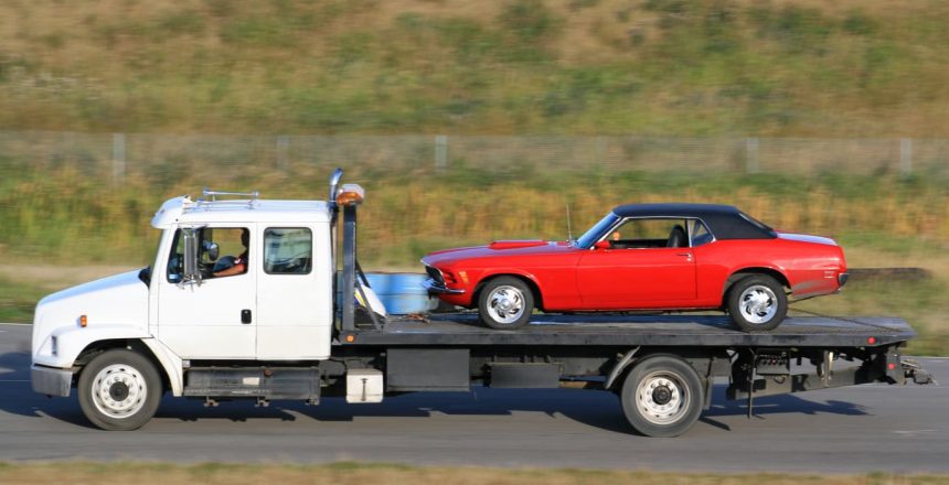 A flatbed tow truck with a classic car during the ship a non-running car process.